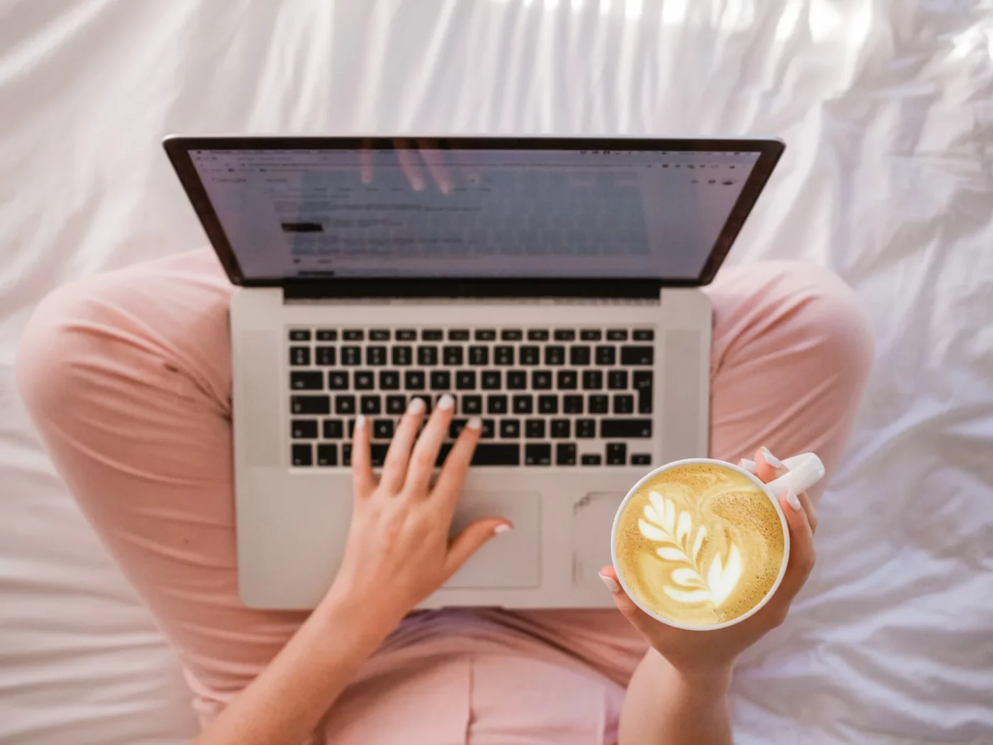 A woman typing on a laptop and holding a cappuccino